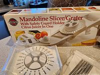 Photo showing closed box of Mandoline Slicer/Grater by Norpro with image of main utensil and citrus juicer attached.