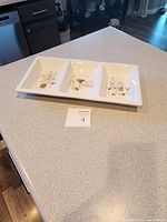 Overhead photo of white ceramic serving tray with three separate square compartments, each featuring different vintage cocktail-themed illustrations.