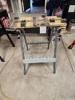 Front view of metal work station showing foldable metal frame and dual wooden slats with clamp mounts.