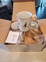 Open box showing one ceramic mug with snowman and Christmas tree design and packaging bubble wrap inside the box