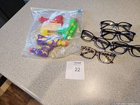 Plastic bag containing four multicolored water toy guns and five pairs of reading glasses with various frame styles.