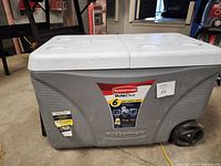Front view of large gray Rubbermaid DuraChill cooler showing brand label and rear wheel on side.