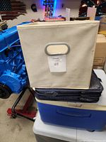 Front view of cream canvas storage cube with plastic-reinforced oval handle, showing item's overall shape and material