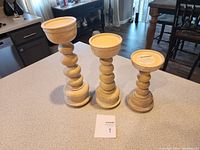Three wooden candle holders of different heights placed on a kitchen counter.