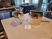 Photo shows pair of vases on counter; one ceramic with gold and cream color, one clear glass with silver bow.