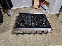 Top-down view showing six burners with cast iron grates on a stainless steel gas range cooktop.