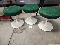 Three vintage swivel stools with green fabric seats and white tulip bases placed on a concrete floor.
