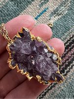 Close-up photo of the amethyst crystal cluster pendant showing the natural crystal formation and gold-tone setting held in hand.