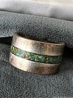 Close-up showing ring's wide sterling silver band with a central inlay of mixed turquoise and visible surface wear and tarnish.