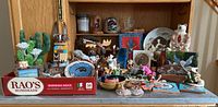Wide view of gathered assorted decorative items on shelf including cacti sculptures, figurines, photo frame, dreamcatchers, and small woodcrafts.