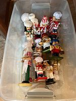 View of two plastic storage tubs filled with various wood nutcracker figurines mainly depicting chefs and holiday characters