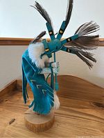 Side angle of Kachina figure showing turquoise costume with white fur and feathered headpiece