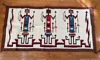 Full view of pictorial wool rug showing entire pattern of three stylized figures and borders lying flat on wooden floor.