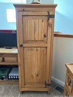 Front view of one pine tall cabinet showing wood grain, raised panel door, and metal hinges/latch hardware.