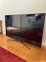 Front view of Samsung 55-inch flatscreen TV showing black bezel and stand on a wood floor.