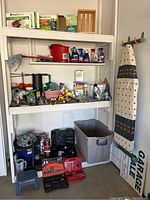 Wide view of shelves with cleaning supplies, household items, a toy truck, and storage bins including an ironing board.