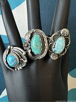 Frontal view of three rings on black stand showing stone colors, bezels and overall condition