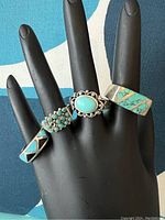 Photo showing four sterling silver turquoise rings on display hand, visible tarnish and wear, with a close view of turquoise stones and ring bands.