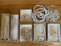 Multiple vintage pearl necklaces in boxes and loosely arranged on a wood surface, showing variety in bead sizes and clasp styles.