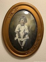 Oval framed black and white portrait of a young child in dress, gold tone frame with floral decorative accents.