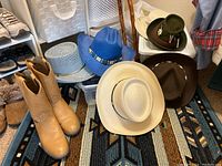 Tan Justin cowboy boots, five cowboy hats on southwestern rug