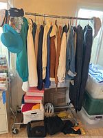Rolling clothes rack with women's coats and jackets hanging, teal wide-brim hat, boxes and bags underneath