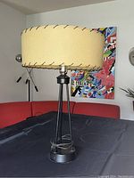 Full view of the 1950s tower style table lamp with rawhide shade on a black surface, showing lamp base and shade.