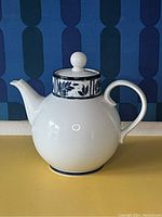 White ceramic Dansk Ceylon teapot with blue decorative band around the neck and matching lid with round knob handle.