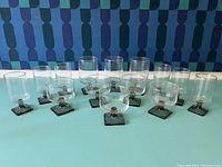 Full set of 11 Nordic smoke grey drinkware glasses with square bottoms displayed against a patterned background.