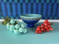 Photo of two grape clusters and one decorative bowl on blue surface with patterned blue background