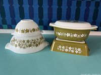 Photo showing stacked large and small Pyrex Cinderella mixing bowls with green Spring Blossom flower band around the center of each, next to oval casserole dish with lid on top of small square casserole dish, both in matching green floral design.
