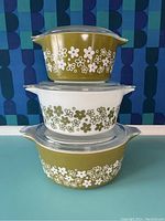 Set of three Pyrex casserole dishes stacked, showing olive green and white floral Spring Blossom pattern