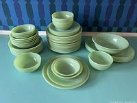 Multiple stacks of jadeite green dinner plates, salad plates, small and medium bowls on a blue surface against a patterned background