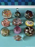Full view of 10 assorted vintage glass paperweights with various internal colors and designs on blue surface