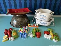 Photo showing the five-piece Cornflower Corelle casserole dishes stacked in metal rack, large brown Texasware mixing bowl, ceramic ashtray, and various ceramic kitchen decor pieces including lobster, vegetables and bottles.