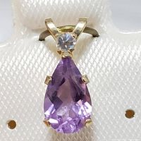 Front view of the pendant showing the pear-shaped purple amethyst and small clear gemstone on 10K yellow gold setting against a white background.