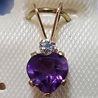 Close-up image of the gold pendant showing the heart-shaped purple amethyst stone and round diamond above it.