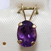 Close-up front view of oval faceted amethyst set in 10K yellow gold pendant with four prongs.