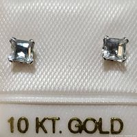 Pair of square cut aquamarine stud earrings in 10K yellow gold on a white textured background with gold text marking 10 KT GOLD