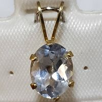 Close-up image showing the oval blue topaz gemstone in a 10K yellow gold six-prong setting on a fabric background.