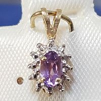 Close-up front view of the pendant showing the oval amethyst center stone surrounded by small diamonds and yellow gold bail.