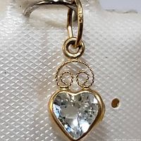 Close-up front and angled views of the heart-shaped blue topaz pendant set in 14K yellow gold with swirl design and bail.