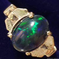 Close-up of oval black opal cabochon set in yellow gold, showing play-of-color