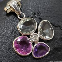 Close-up front view of pendant showing the four fancy color sapphires and central diamond set in 14K white gold.