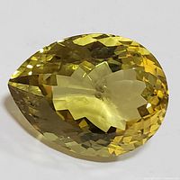 Front-side view of pear-shaped lemon quartz gemstone showing yellow hue and faceted cut.