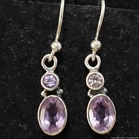 Close-up photo of one sterling silver earring with two bezel-set amethyst stones, one round and one oval.