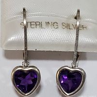 Front view of both sterling silver heart-shaped amethyst earrings hanging on display card marked 'STERLING SILVER'