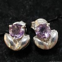 Close-up photo of pair of sterling silver earrings with round purple amethyst stones and petal-shaped silver base.