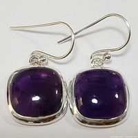 Pair of sterling silver earrings featuring polished rounded square amethyst stones set in bezel with hook style backs, shown from front.
