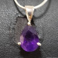Close-up of pear-shaped faceted purple amethyst pendant set in sterling silver with silver chain on a black background.